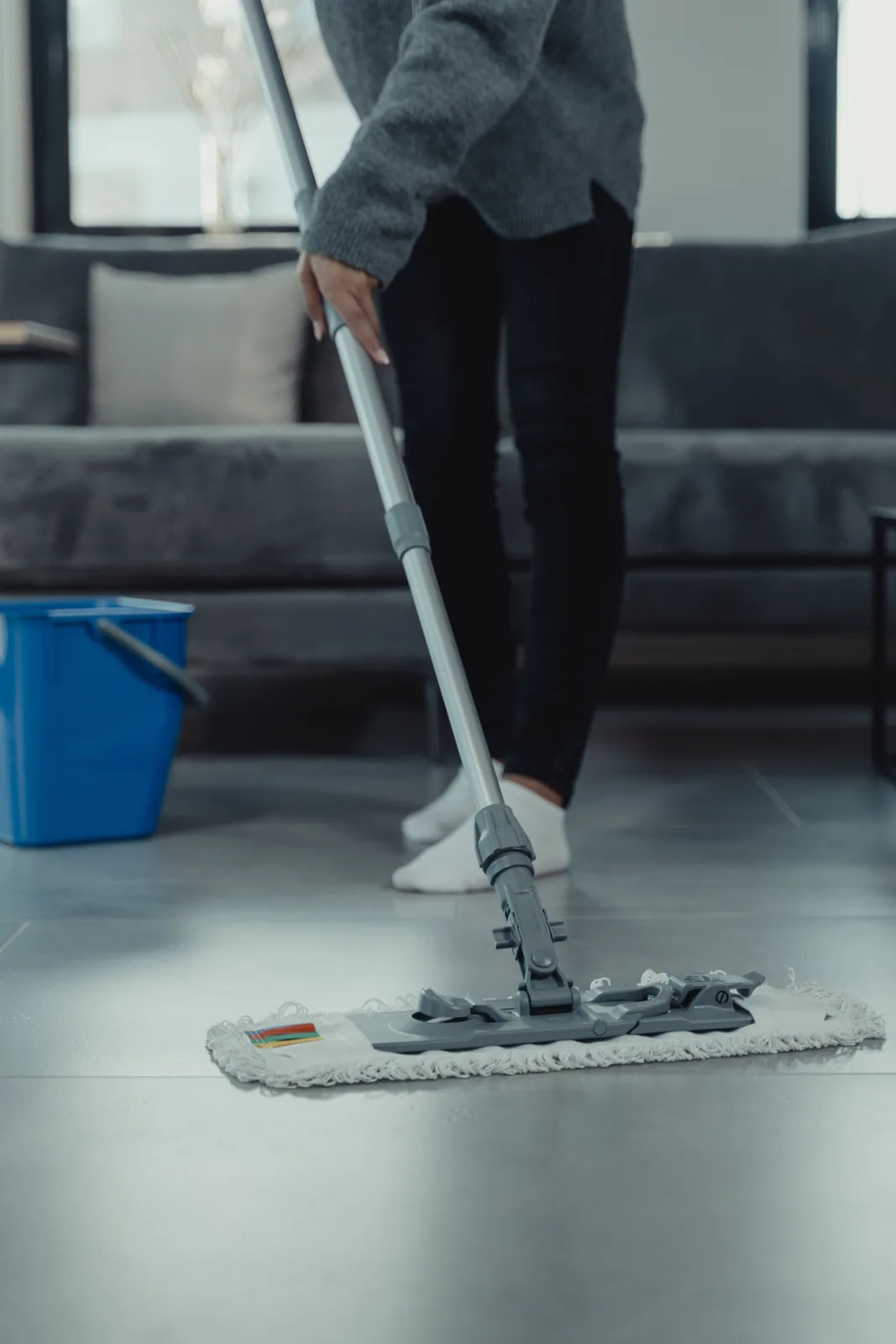 A cleaner mopping a living-room floor beside a sofa