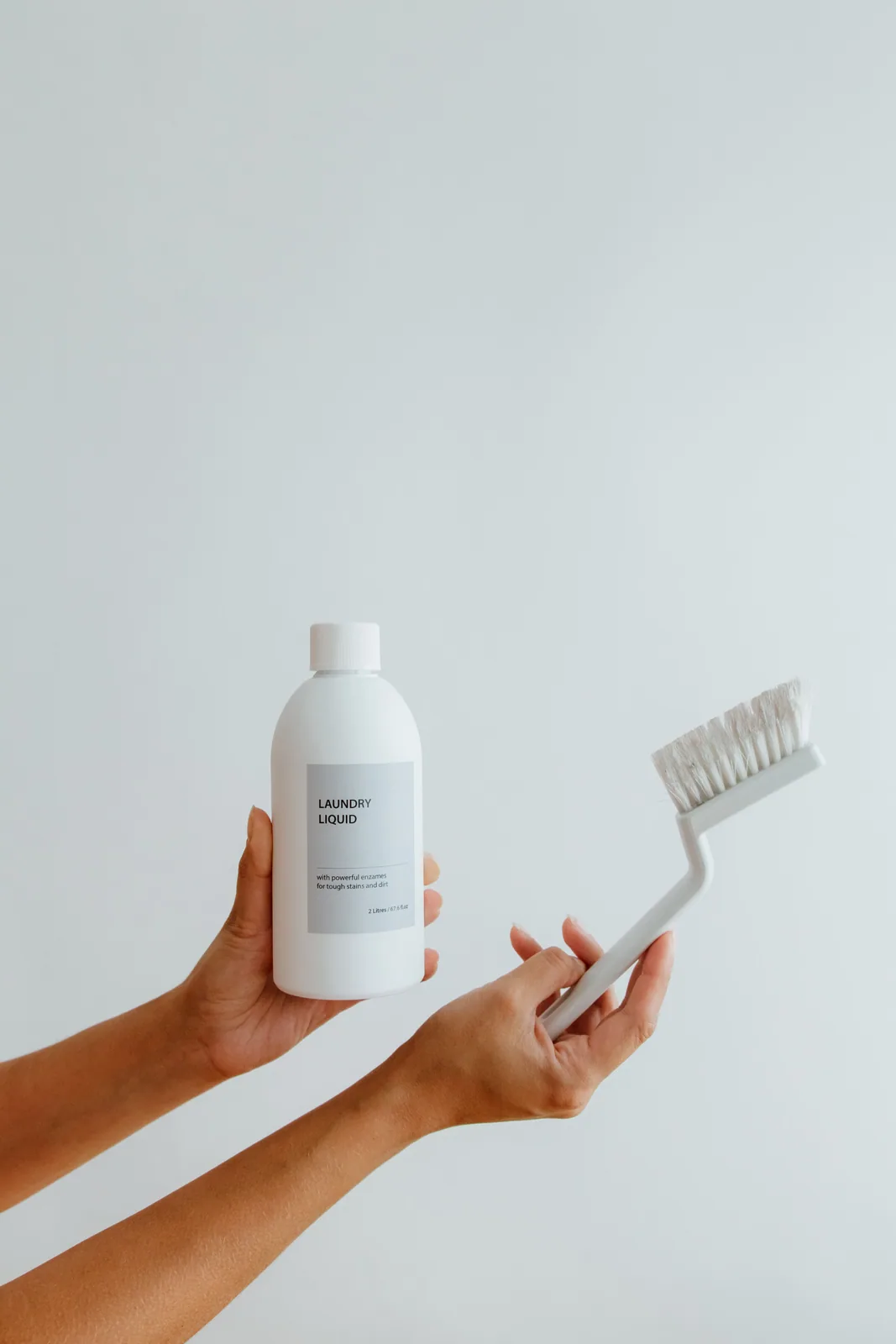 Hands holding a bottle of cleaning liquid and a scrubbing brush
