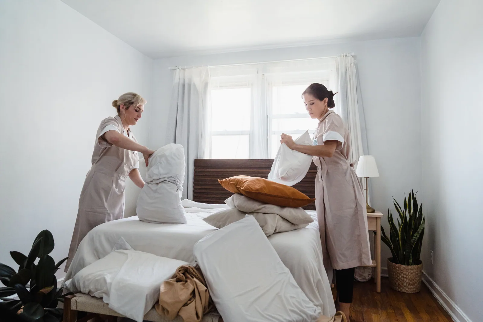 Two cleaners making up a bed with fresh white linen