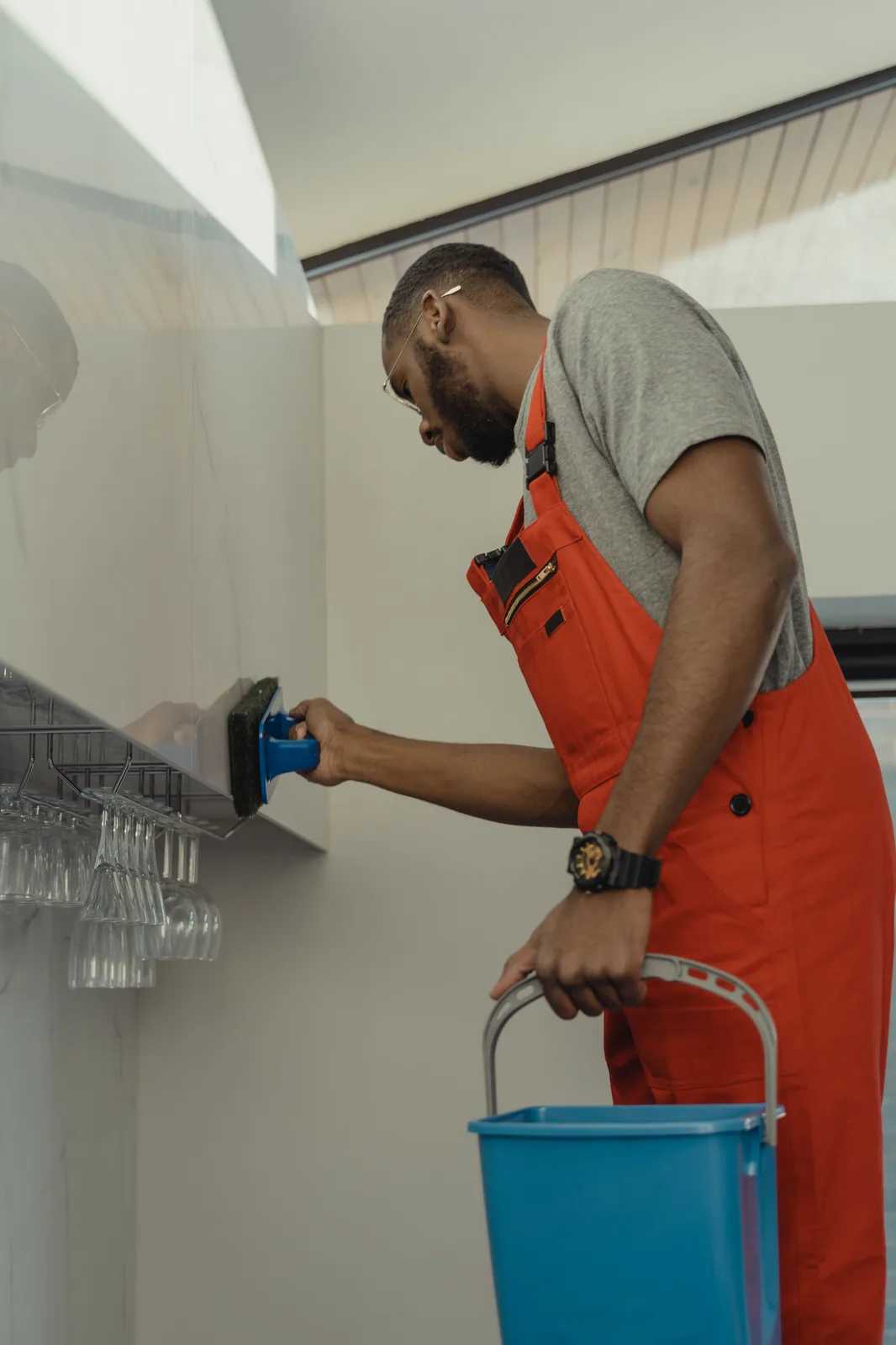 A cleaner scrubbing a glass shelf above a rack of polished glassware