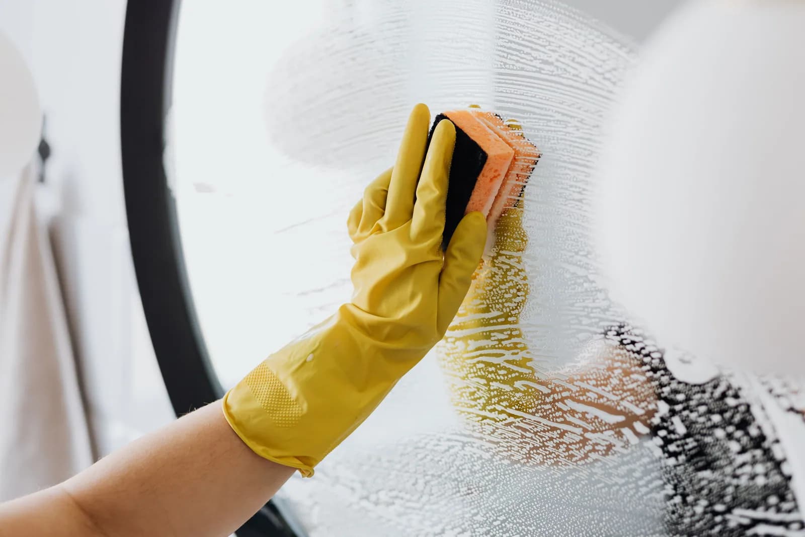 A sponge cutting a clear stripe through heavy suds on a mirror